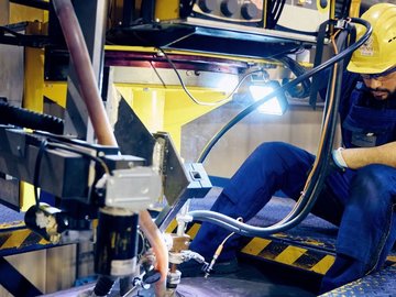 Arbeiter in Schutzkleidung und Helm bedient eine große industrielle Maschine in einer Produktionshalle.